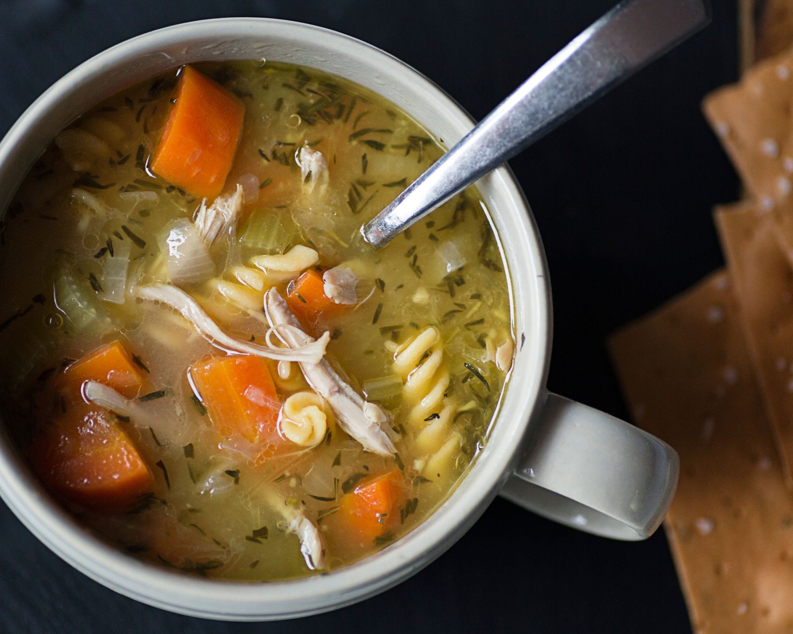 Chicken noodle soup in a mug with a spoon. Temporary concept photography.