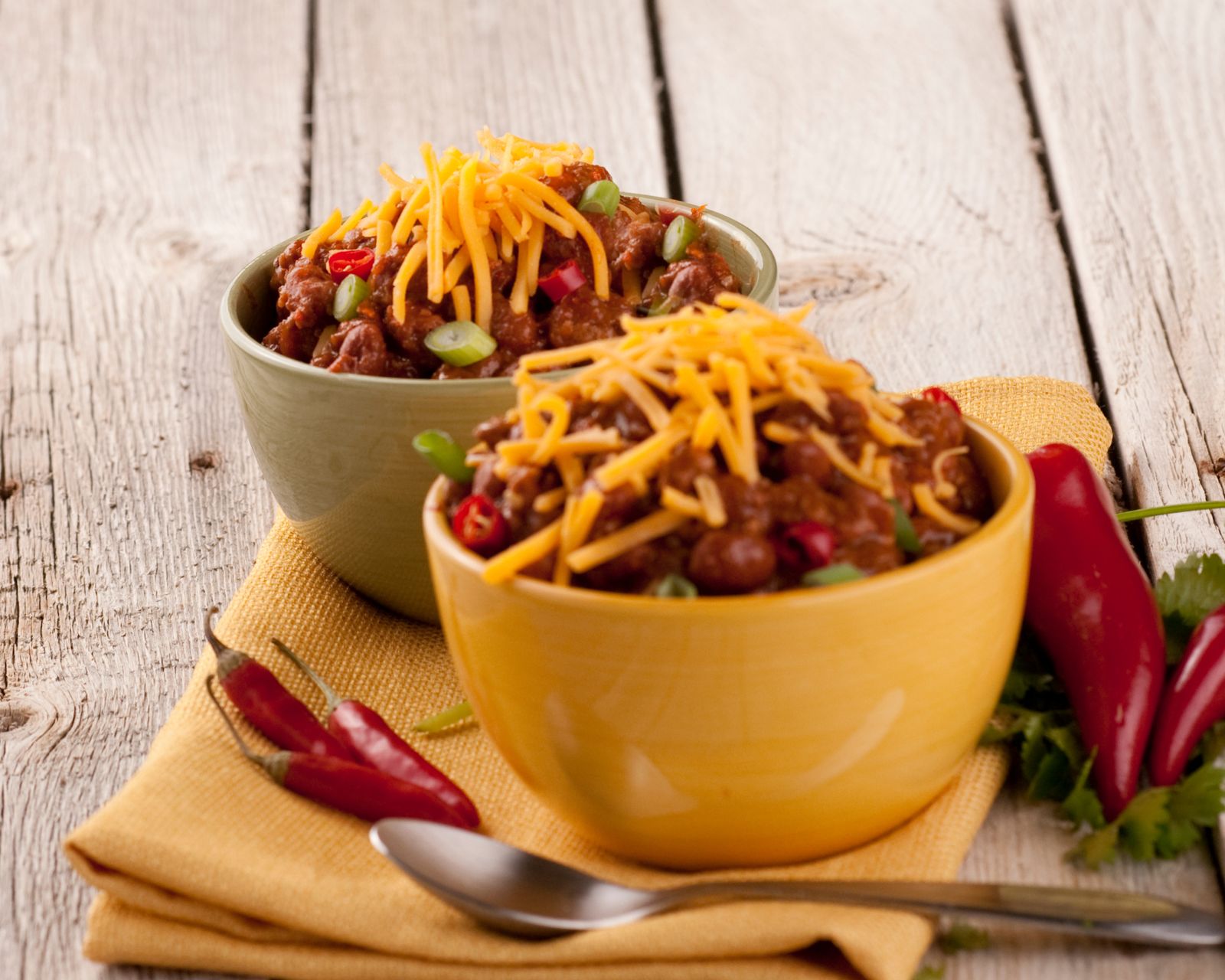 Two bowls of chili with cheese and chili peppers nearby. Temporary concept photography.
