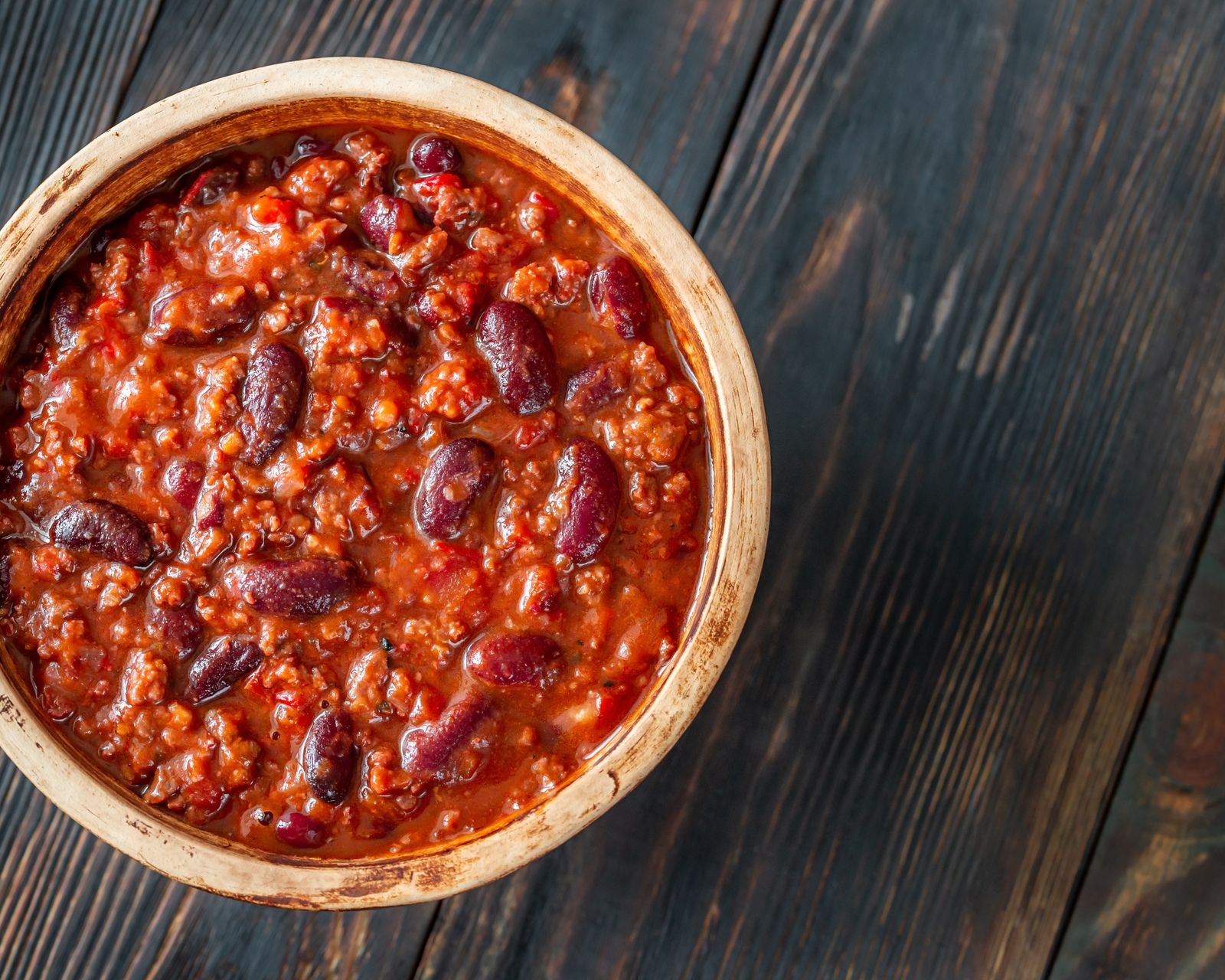 A bowl of chili on a dark wood table. Temporary concept photography.