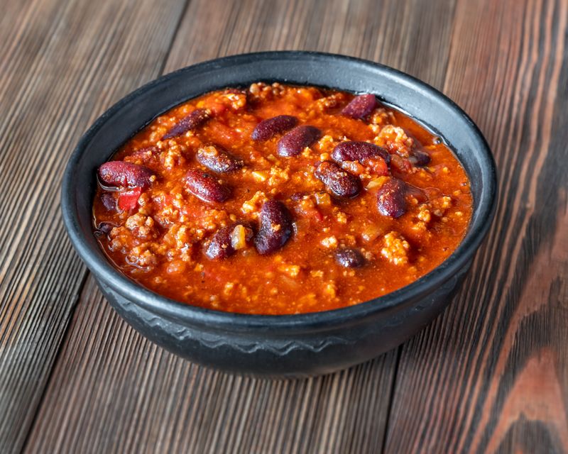 Chili in a black bowl on a wood table. Temporary concept photography.